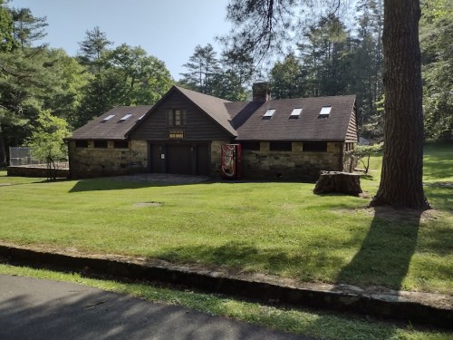 A rustic stone building with a sloped roof, surrounded by green grass and trees in a serene outdoor setting.
