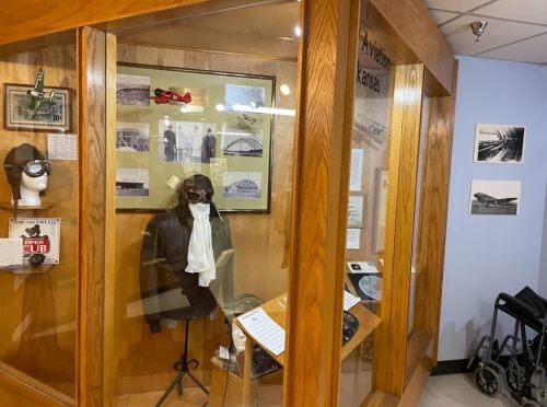 Display case featuring aviation artifacts, including a pilot's outfit, photographs, and model airplanes.