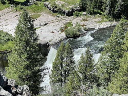 A scenic view of a waterfall cascading into a river, surrounded by lush greenery and rocky terrain.