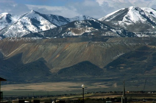 Snow-capped mountains rise above a valley, showcasing rugged terrain and a clear blue sky.