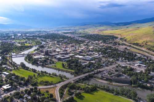 Aerial view of a city surrounded by green hills and rivers, showcasing urban development and natural landscapes.