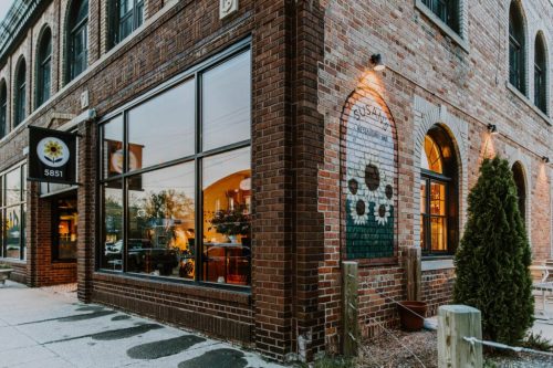 A brick building with large windows, featuring a mural of sunflowers and a sign for "5851" on the corner.