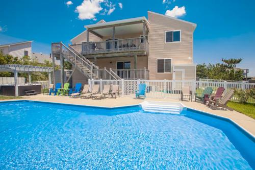 A sunny backyard with a blue pool, lounge chairs, and a two-story house in the background under a clear blue sky.