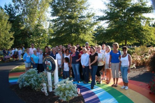 A diverse group of people poses together in a colorful garden, smiling in front of a sign.
