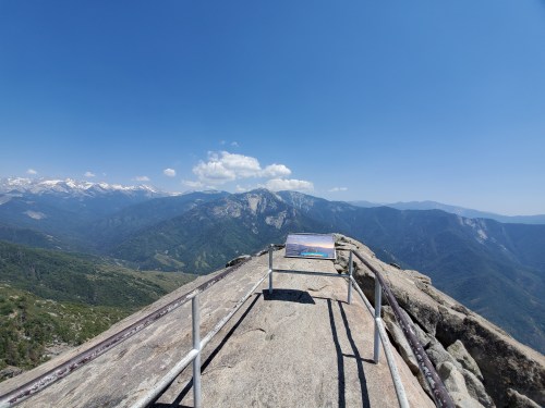 A panoramic view from a rocky overlook, showcasing mountains and valleys under a clear blue sky.