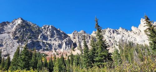 A scenic view of rugged mountains under a clear blue sky, surrounded by lush green trees.