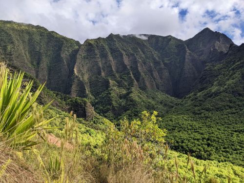 Lush green mountains with steep ridges under a partly cloudy sky, surrounded by dense vegetation.