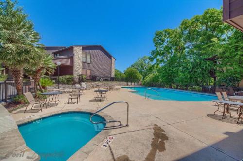 A sunny pool area with two swimming pools, lounge chairs, and lush greenery in the background.
