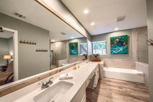Modern bathroom with a double vanity, large mirror, shower, bathtub, and green walls adorned with nature-themed artwork.