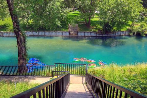A serene river scene with steps leading down to clear blue water, surrounded by lush greenery and colorful floating objects.