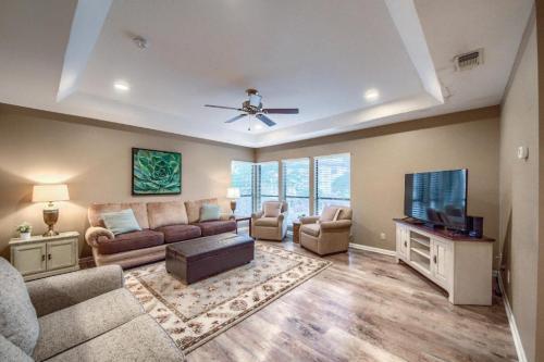 Cozy living room with beige sofas, a coffee table, TV, and large windows, featuring warm lighting and a decorative plant.