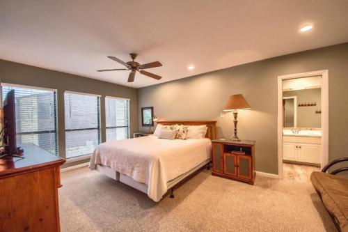 Cozy bedroom with a queen bed, ceiling fan, dresser, and en-suite bathroom, featuring large windows and soft lighting.