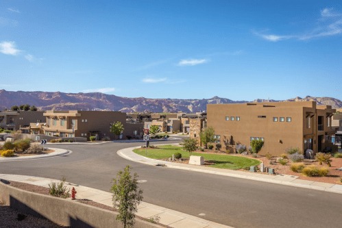 A scenic view of a residential neighborhood with modern homes, surrounded by mountains and clear blue skies.