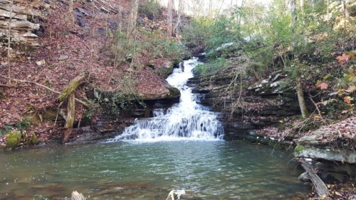 A serene waterfall cascading into a calm pool, surrounded by rocky terrain and autumn foliage.