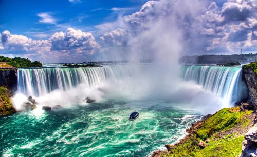 A stunning view of Niagara Falls with cascading water, mist, and a boat on the turquoise river below.