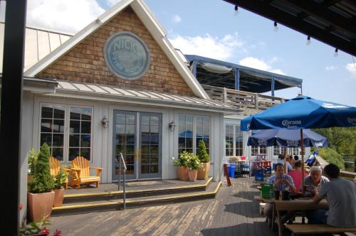 A waterfront restaurant with a wooden exterior, outdoor seating, and umbrellas, bustling with diners on a sunny day.