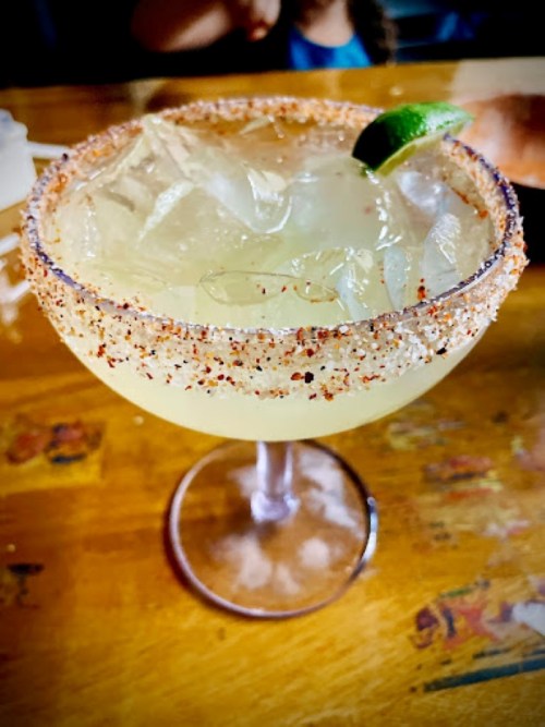 A close-up of a margarita in a glass with a salted rim, garnished with a lime wedge, on a wooden table.