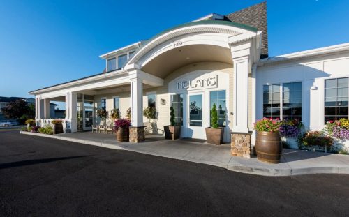Exterior of a charming building with a welcoming entrance, surrounded by flowers and decorative barrels.