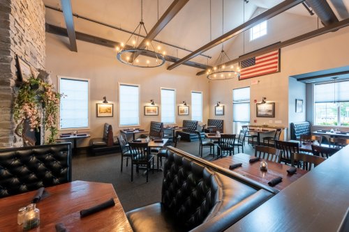 Interior of a restaurant featuring dark wood tables, black leather seating, and an American flag on the wall.