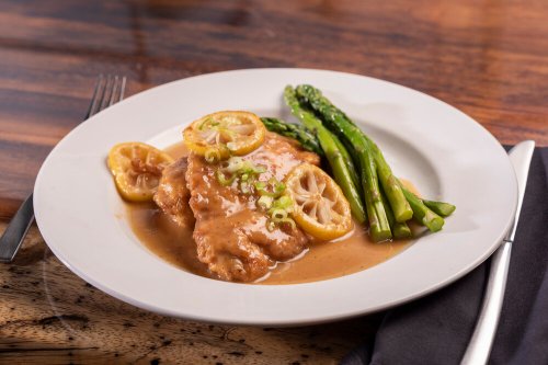 A plate of lemon chicken with asparagus, garnished with lemon slices and green onions, on a wooden table.