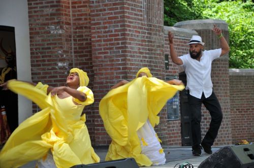 Two dancers in yellow dresses perform energetically on stage, accompanied by a man in a white shirt and black pants.