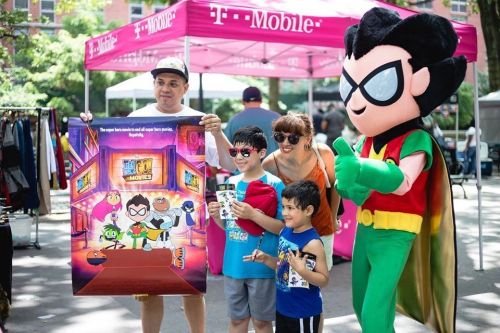 A family poses with a costumed character at a T-Mobile event, holding a colorful poster and enjoying the day.