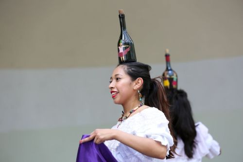 A dancer balances a bottle on her head while performing, wearing traditional attire and colorful accessories.