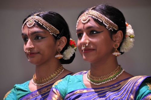Two women in traditional Indian attire, adorned with jewelry and floral hair accessories, smiling gracefully.
