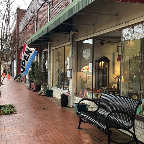 A quaint street scene with a bench, an "OPEN" flag, and storefronts under a cloudy sky.
