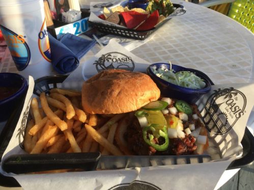 A plate with a sandwich, fries, coleslaw, and jalapeños on a table at a restaurant.