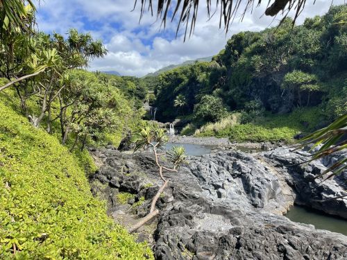 Lush green landscape with rocky terrain and a small waterfall in the background under a partly cloudy sky.