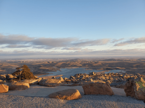 A scenic view of a vast landscape with a lake, rocky terrain, and a clear sky during sunset.