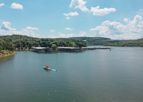 A serene lake scene with a small boat near a dock, surrounded by green hills and fluffy clouds in a blue sky.