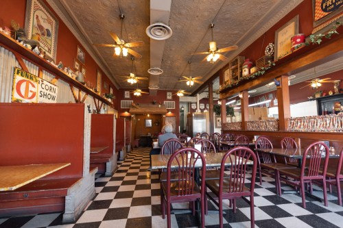 A cozy restaurant interior with checkered floors, wooden tables, and vintage decor, featuring ceiling fans and booths.