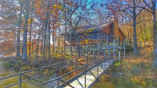 A wooden cabin surrounded by trees, with a walkway leading to the water, showcasing autumn foliage.
