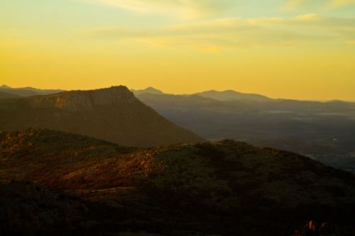 Sunset over rolling hills and mountains, casting warm golden hues across the landscape.