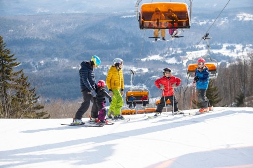 A family enjoys skiing on a snowy slope, with ski lifts in the background and mountains in the distance.