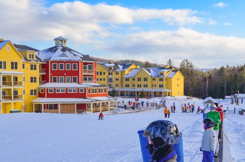 Colorful ski resort buildings with people skiing and enjoying winter activities on a snowy landscape.