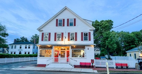 A charming white building with red accents, featuring a café and bakery, surrounded by trees and a picket fence.