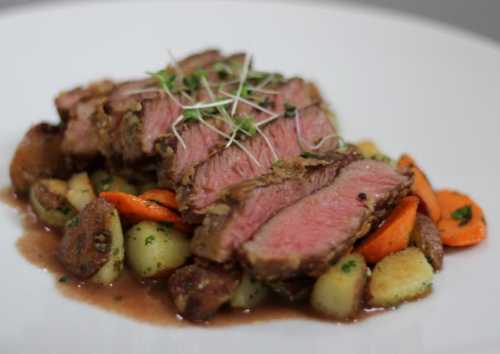 Sliced roast beef served on a bed of roasted vegetables and garnished with microgreens.