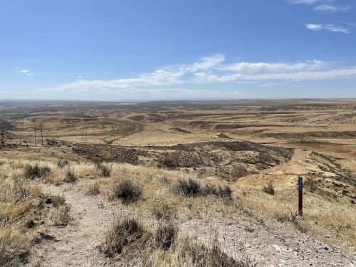 A vast, dry landscape with rolling hills and a winding river under a clear blue sky. Sparse vegetation covers the ground.