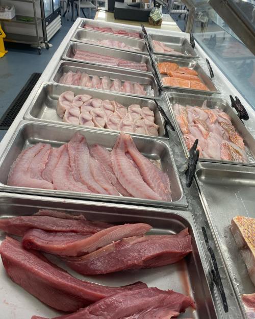 A display of various fish fillets and seafood in metal trays at a market.