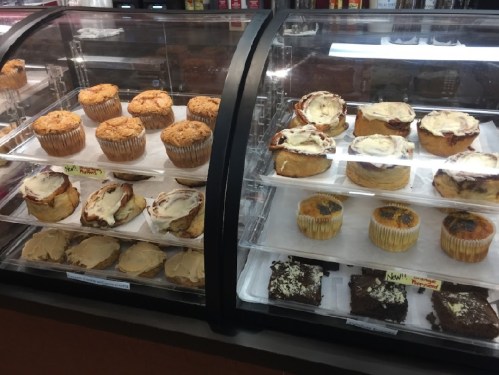A display case filled with various baked goods, including muffins, cinnamon rolls, and brownies.