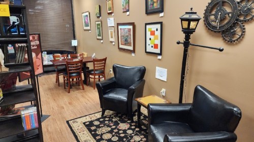 Cozy café interior with black chairs, a lamp post, artwork on the walls, and a small dining area in the background.