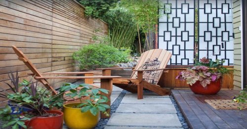A serene outdoor space featuring wooden chairs, colorful potted plants, and a decorative screen amidst lush greenery.