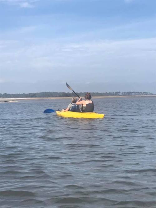 Two people kayaking on a calm body of water under a clear blue sky.