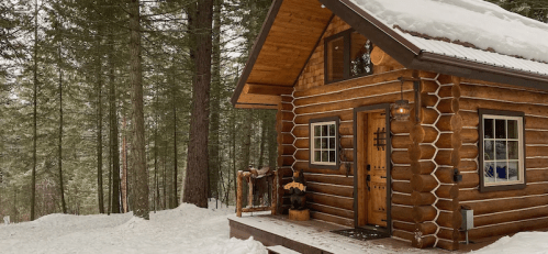 A cozy log cabin surrounded by snow-covered trees in a winter landscape.