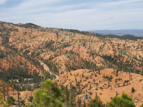 A scenic view of orange-hued hills and pine trees under a partly cloudy sky.