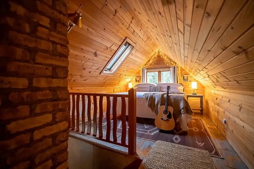 Cozy attic bedroom with wooden walls, a bed, guitar, and warm lighting, creating a welcoming atmosphere.
