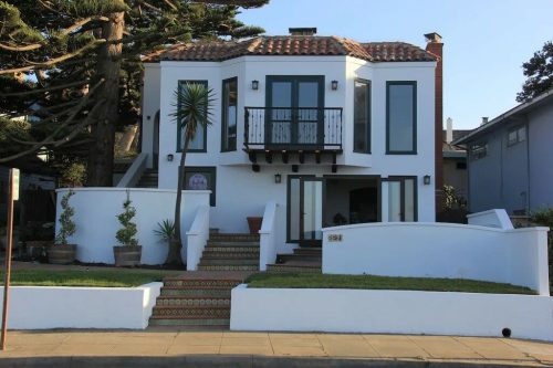 A modern white house with a tiled roof, large windows, and a landscaped front yard.